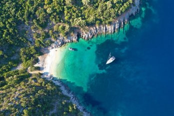 Aerial shot of a sailboat anchored in a small bay on an island with the ocean