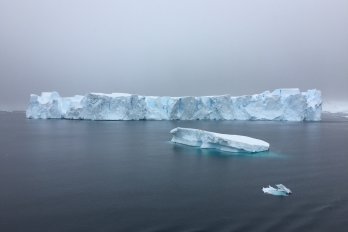 long, low iceberg floating on dark grey sea with gloomy, dark, overcast sky in background