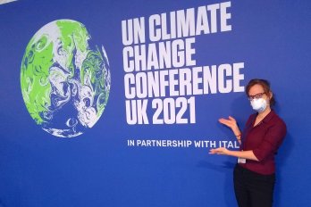 PhD Student Shaina Sadai stands in front of a blue wall with white letters and a globe on it.  The text reads: "UN Climate Chang