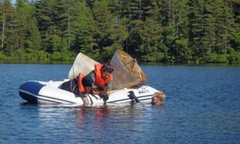 Dan Miller, Helen Habicht, and Benjamin Keilsing in an inflatable boat on a wooded lake, recovering sediment traps...