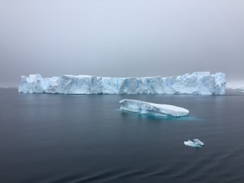 long, low iceberg floating on dark grey sea with gloomy, dark, overcast sky in background