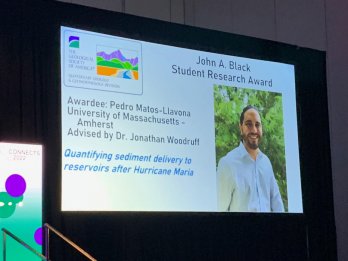 Photograph of slide projected onto a screen at a conference with Pedros' picture and title of award and research