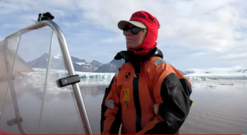 Picture of Dr. Julie Brigham-Grette piloting a small boat in an icy ocean with snowy mountains in the background.