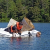 Dan Miller, Helen Habicht, and Benjamin Keilsing in an inflatable boat on a wooded lake, recovering sediment traps...