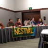 6 students seated, panel style, at table in hotel conference room, facing camera, with large banner displaying letters 'NESTVAL' draped over front of table.