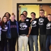 Members of U-Mass Geography club assembled for group photo in front of doorway in lecture all, smiling at camera and wearing Geography Club t-shirts