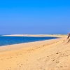 Orange-yellow sand with a small beach bluff, deep blue water and sky: a perfect summer day in Provincetown, MA