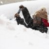 A woman shovels snow off her car, not visible under the piles