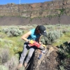 Karin Legnick in steep sided open canyon using a power tool on a boulder.
