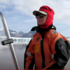 Picture of Dr. Julie Brigham-Grette piloting a small boat in an icy ocean with snowy mountains in the background.