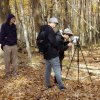 Three masculine presenting students in the woods using a plane table survey transit and taking notes.