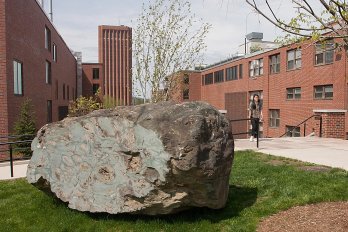 Car-sized boulder of pillow lava sitting on lawn between two brick buildings built as fallout shelters in the 1950s.