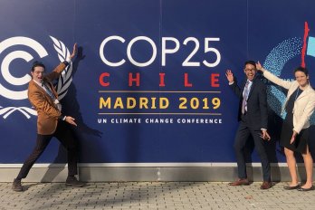 Dr. Benjamin Keisling, Dr. Julian Reyes, and Hannah Baranes, all in formal attire, striking poses in front of wall with dark blue COP25 logo.