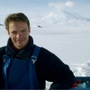 Portrait of Dr. Rob Deconto, smiling at camera in front of white snow field, with volcano in backrgound, in Antarctica