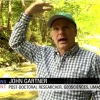 Screen capture of post-doc John Gartner speaking to camera in front of Chicklea River in Hawley, MA. John is gesturing to show height of floodwaters above his head.
