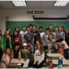 Over a dozen members of the U-Mass Geography club posing for a group photo within a classroom.