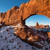 Orange sandstone rock arch in snowy desert landscape with clear blue sky (Turret Arch)